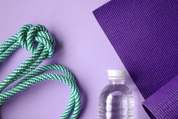 健身器材。瑜伽垫，跳绳，水在紫罗兰背景。平的。健康的生活方式和锻炼理念。图片下载