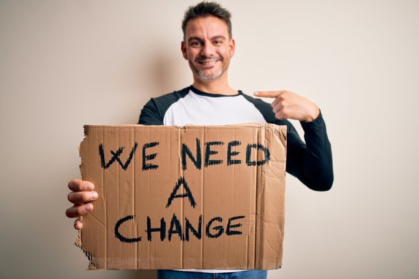 年轻英俊的激进分子男子举着旗帜与改变信息在粉红色的背景与惊讶的脸指向自己图片下载