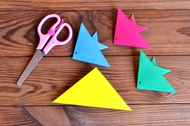 折纸五彩鱼，剪刀。为孩子们准备的暑期工艺品。如何为孩子们制作纸鱼工艺品。布朗木制背景图片下载
