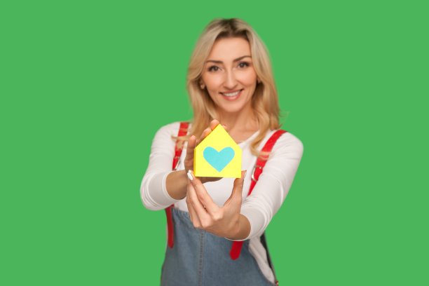 购房，房地产保险。肖像快乐美丽的成年金发女人在城市风格的工装裤展示纸房子图片下载