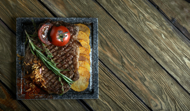 用刀叉雕刻在黑色石板上的烤牛排。在滚烫的大理石上烤牛排。复制空间，深色背景，美食时尚照片图片下载