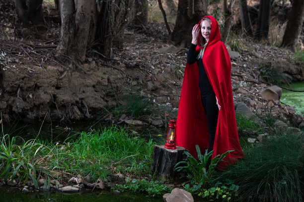 一个迷人的女人戴着小红帽，提着灯笼在黑暗的森林里穿过一条小溪图片下载