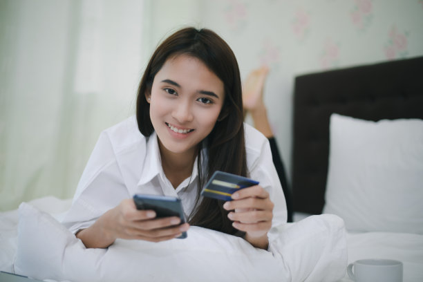 亚洲女性在网上购物和在手机上用信用卡付款。亚洲女性在网上购物和在手机上用信用卡付款。快乐的女人在床上上网图片下载