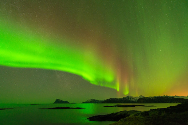 这是一张山水照片，有美丽的绿色北极光，在黑暗的星星点缀的天空中反射在海洋中图片下载