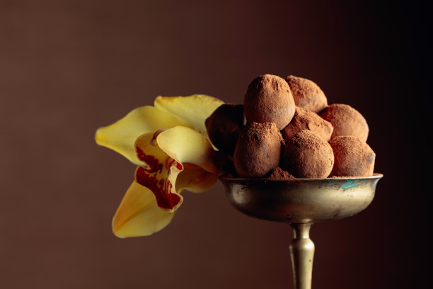 古铜色花瓶里的巧克力松露，洒上可可粉，饰以兰花。图片下载