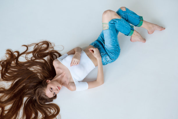 美丽的特写肖像美丽的女性的脸与长棕色的头发躺在白色。头发护理的概念。图片下载