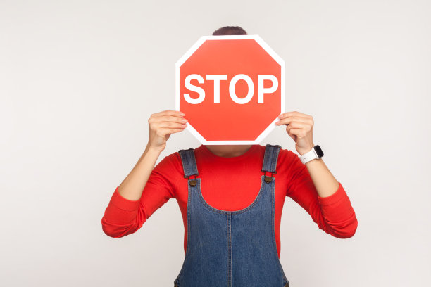 注意,禁区!女人在牛仔工作服覆盖脸八角形停止标志，显示红色交通标志图片下载