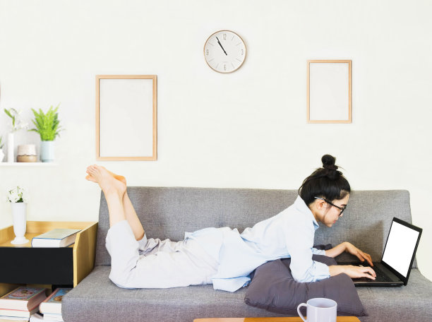 年轻美丽的亚洲女人穿着蓝色的衬衫，坐在灰色的沙发上，在线工作的生活方式，放松在家里的咖啡杯，在家工作笔记本电脑，在家工作图片下载