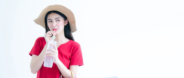 肖像快乐的年轻亚洲妇女在红色的裙子和针织帽饮用水，而手持购物袋孤立在白色的背景。图片下载