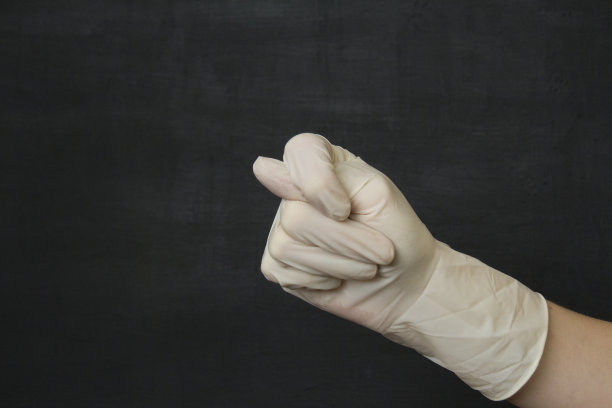 一只手在白色医用一次性橡胶乳胶手套显示一个无花果在黑色的背景。一次性防护手套可以防止病毒、冠状病毒和危险细菌图片下载