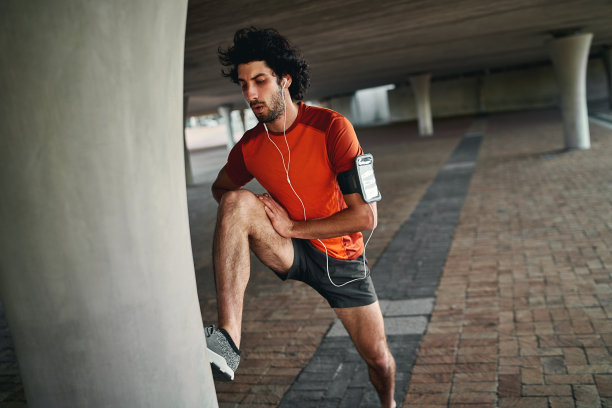 一个健康迷人的年轻男子的肖像，听着音乐耳机伸展他的腿，然后去桥下跑步图片下载