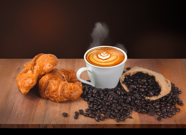 热咖啡、咖啡豆和羊角面包放在一张黑色和红色背景的旧木桌上。图片下载