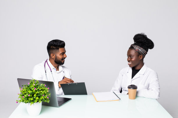 两位医生在办公室开会时一起讨论新的治疗方法的照片。医生一边使用台式电脑一边讨论新的治疗方法。图片下载