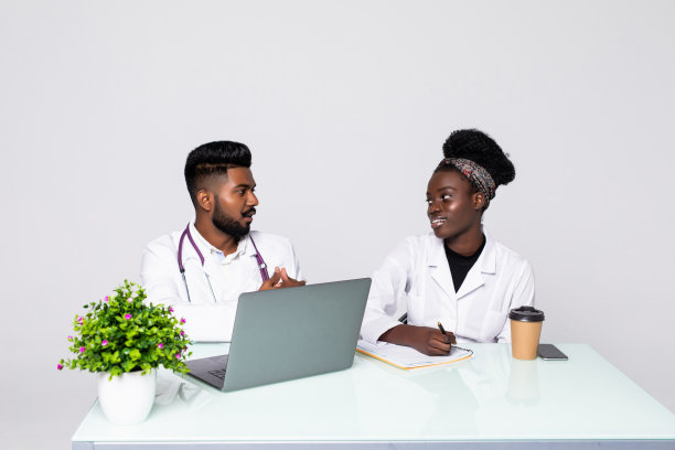 两位医生在办公室开会时一起讨论新的治疗方法的照片。医生一边使用台式电脑一边讨论新的治疗方法。图片下载