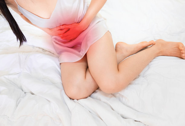 一个女人穿着白色的睡衣躺在床上，肚子痛。一个女人的肠子有急性炎症，手拿着肚子痛的斑点。概念照片，读取点指示疼痛的位置，图片下载