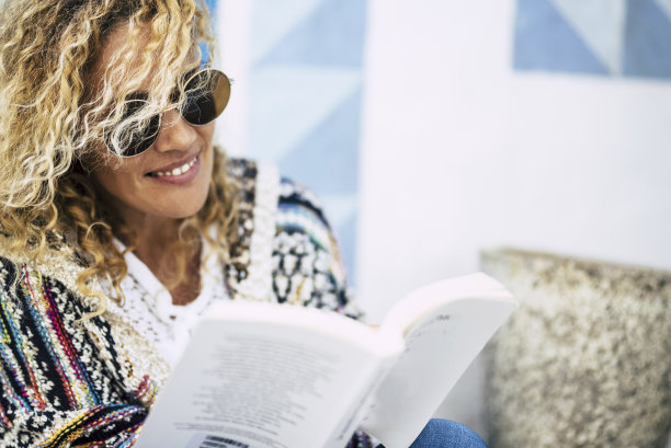 美丽的白种人金发女人的肖像阅读纸书户外-白色和蓝色的墙壁背景-成年人学习和享受户外休闲活动图片下载