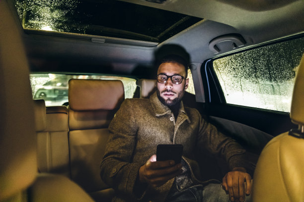 年轻的成年男子在汽车库存照片的后座上使用手机图片下载
