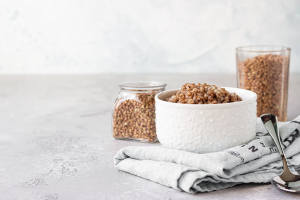 陶瓷碗与美味的煮荞麦和有机生荞麦谷物玻璃。浅灰色混凝土背景。图片下载