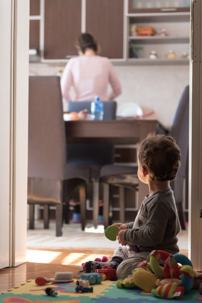 孩子坐在门口玩玩具，而母亲在厨房做饭图片下载