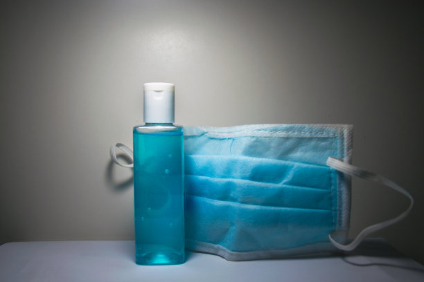 预防冠状病毒感染所需的一瓶洗手液和医用口罩，放置在白色桌子和白色背景上图片下载