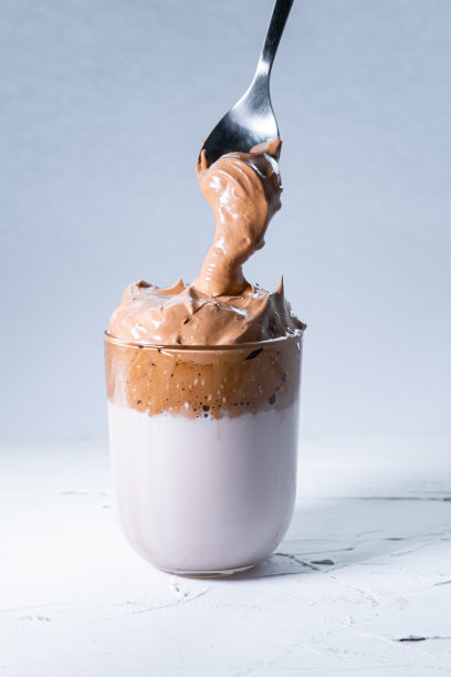 奥利安达尔戈纳咖啡和勺子奶油咖啡落入一个玻璃在白色的背景。垂直的照片。图片下载