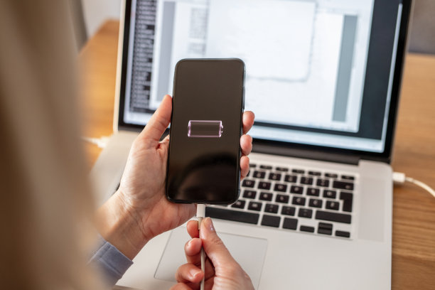 一个女人用笔记本电脑的USB线给已经报废的智能手机充电图片下载