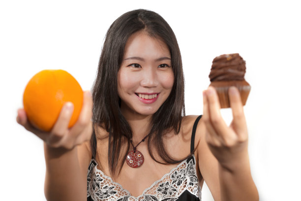 年轻迷人、快乐的亚洲中国女人拿着美味诱人的巧克力纸杯蛋糕，里面充满了卡路里和新鲜健康的橙子，低卡路里，而不是含糖的垃圾食品图片下载