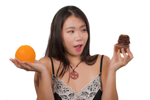 年轻有魅力和快乐的亚洲韩国女人拿着美味和诱人的巧克力纸杯蛋糕充满卡路里和新鲜健康的橙子低卡路里，而不是含糖的垃圾食品图片下载