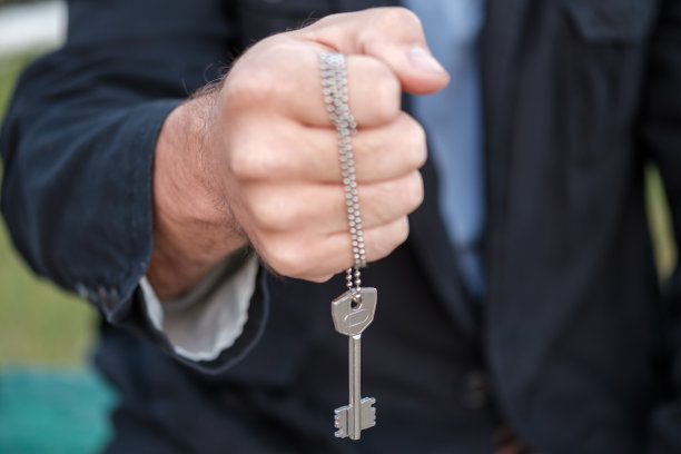 一个穿着黑夹克的男人的手递过一个挂在链子上的钥匙图片下载