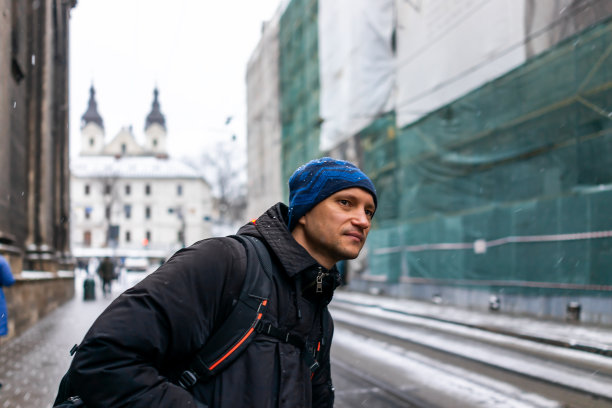 在乌克兰利沃夫老城区附近的集市广场上，冬日里利沃夫带着圣诞的寒冷大雪和背包旅行的男人在公交车站等车张望图片下载