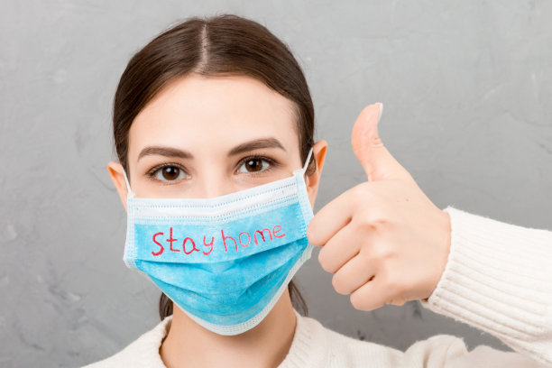 戴着医用口罩的年轻女子的肖像在灰色的水泥背景下呆在家里。人是快乐的，因为她终于健康了。保护你的健康。冠状病毒自我隔离概念图片下载
