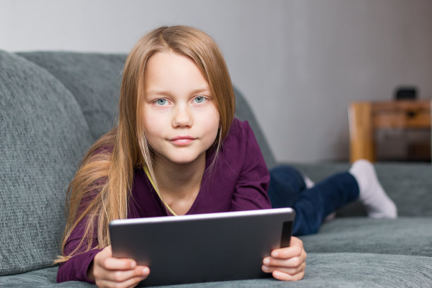 一个女孩躺在沙发上，手里拿着一个平板电脑图片下载