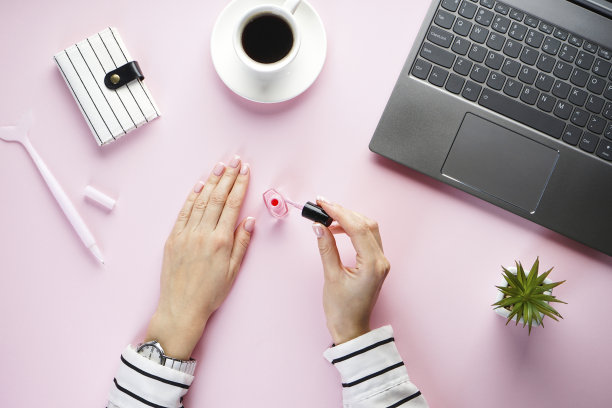 一个美丽的小女孩的手在一个粉红色的背景上，一个笔记本电脑，一杯咖啡和一个粉红色的笔和一个条纹笔记本。平的。图片下载