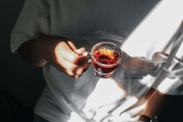 近的人从茶壶倒热茶到小玻璃靠近窗户。泡茶的过程，茶道，一杯刚泡好的黄色或绿色的香草茶，光线温暖柔和，心情阴郁。杯内液体运动图片下载