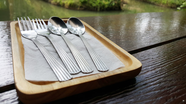 在森林浮动市场美食餐厅的深棕色餐桌上，长方形的木制托盘上，双对餐具银器勺子叉子，平面设计组件图片下载