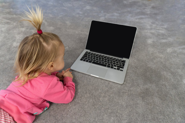可爱的金发白种人小孩躺在地板上灰色的地毯上，在笔记本电脑上看卡通片。黑屏，模型，拷贝空间，顶部视图。图片下载