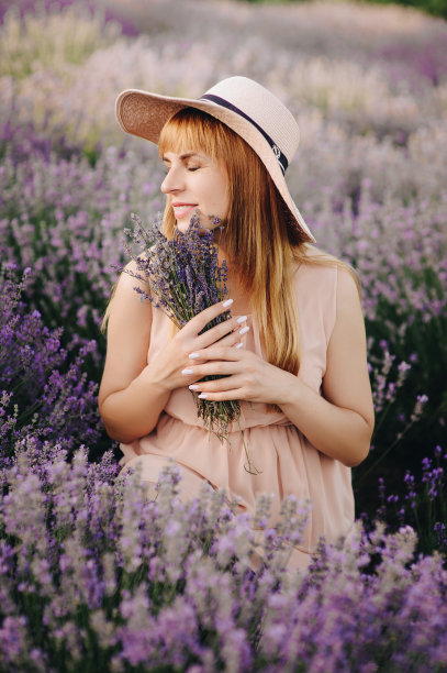 怀孕的金发女孩，米黄色的衣服和草帽。薰衣草。期待孩子的到来。拍摄照片的想法。走在日落时分。未来的妈妈。肖像。束鲜花。图片下载