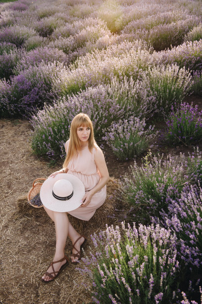 怀孕的金发女孩，米黄色的衣服和草帽。薰衣草。期待孩子的到来。拍摄照片的想法。走在日落时分。未来的妈妈。篮子里的花。图片下载