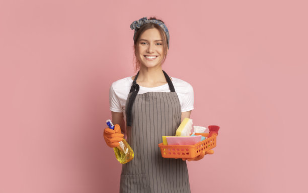 快乐的家庭主妇用洗涤剂喷雾和清洁工具在粉红色的背景图片下载