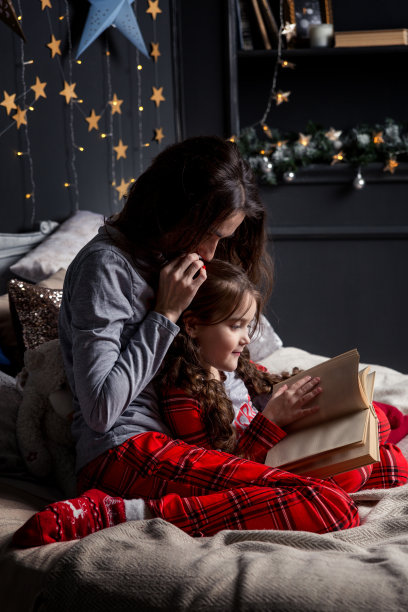 妈妈拥抱她的女儿，在床上给她读一本书。图片下载