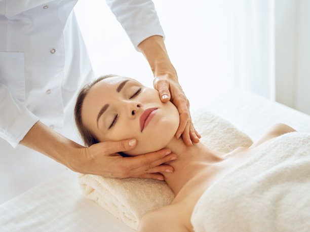 一位闭着眼睛享受面部按摩的美女。医学中的水疗治疗理念图片下载