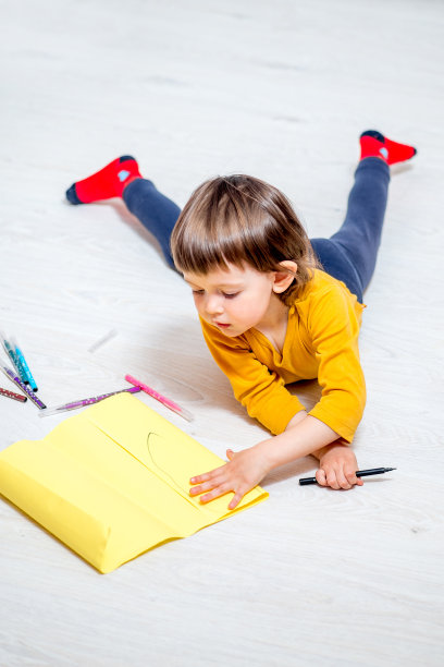 孩子拿着放在地板上的毡头笔在纸上画画图片下载