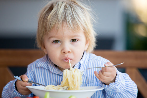 可爱的孩子，蹒跚学步的金发男孩，在花园里吃意大利面图片下载