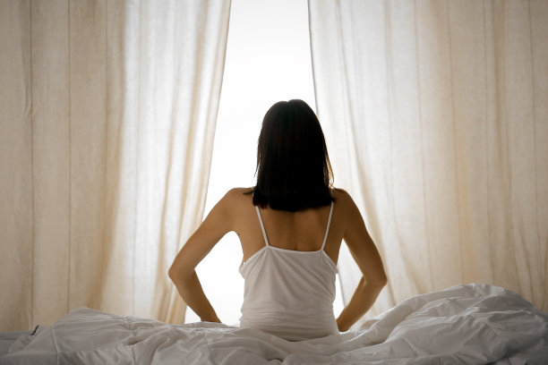 女人在床上伸开双手醒来后，太阳耀斑。深色头发的女人进入一个愉快和放松的一天后，睡了一个好觉和后视图。崭新的一天和快乐的周末图片下载