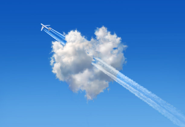 蓝色天空中心形的蓬松云，一架大型喷气式飞机在云中飞过，象征着爱的箭头。图片下载