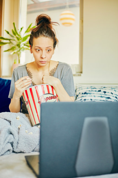可爱的女人在家吃爆米花看电影。图片下载