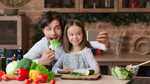 快乐的爸爸用智能手机自拍，小女儿在厨房里图片下载