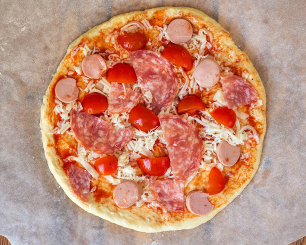 收获自制披萨。生披萨配香肠，香肠和西红柿图片下载