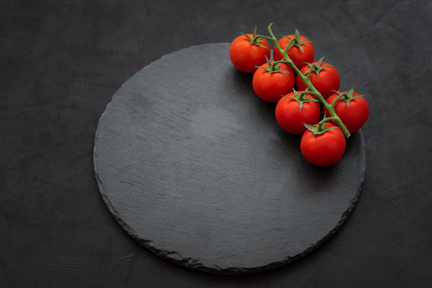 俯视图新鲜的红色樱桃西红柿在黑暗的石头背景。模板用空圆板板。烹饪、健康饮食或素食的概念图片下载