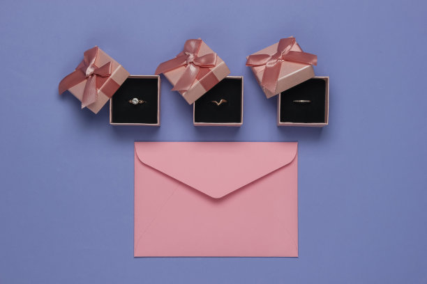 金戒指装在礼品盒里，信封上有紫色背景的婚礼请柬。前视图。平躺图片下载